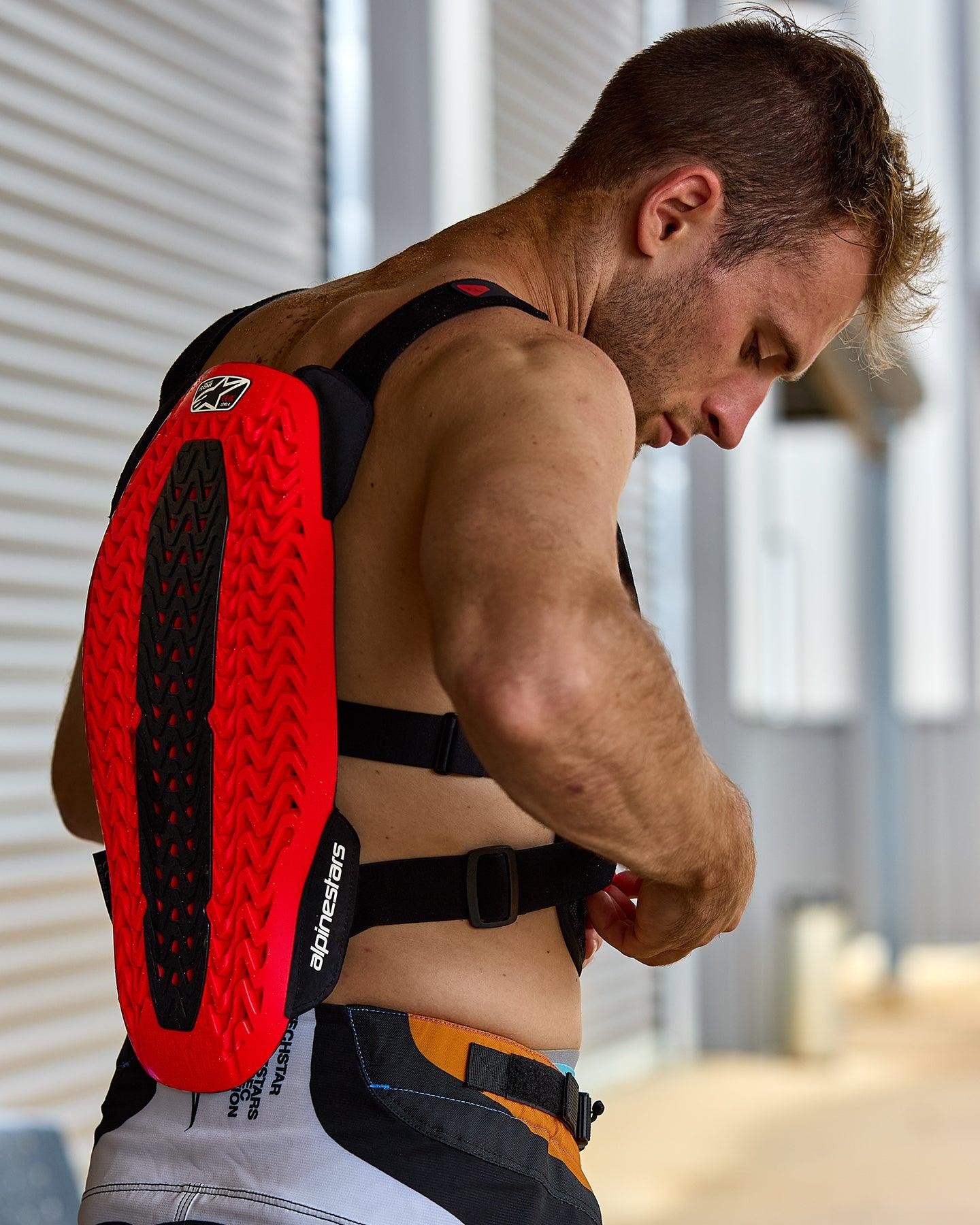 Protector de pecho Alpinestars A-5 Plasma, rojo y negro, con un protector de espalda texturizado con tecnología Nucleon PLASMA, usado por un hombre ajustando las correas negras, vista lateral que destaca la carcasa protectora y el diseño flexible para conducción off-road
