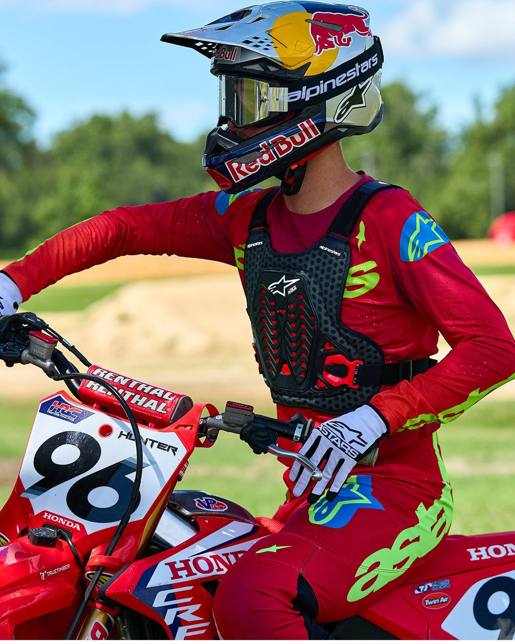 Piloto de motocross con el protector de pecho Alpinestars A-5 Plasma en negro y rojo, combinado con jersey y pantalones de carreras en rojo y verde lima, sentado sobre una motocicleta Honda roja, equipo de protección off-road de alto rendimiento