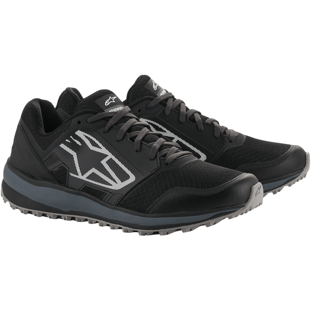 Alpinestars Meta Trail Shoes, zapatillas de running de alto rendimiento, negro y gris oscuro, gran logotipo Astars blanco con rayas en el lateral, diseño con cordones y suela gris robusta, diseñadas para brindar comodidad durante todo el día en el paddock