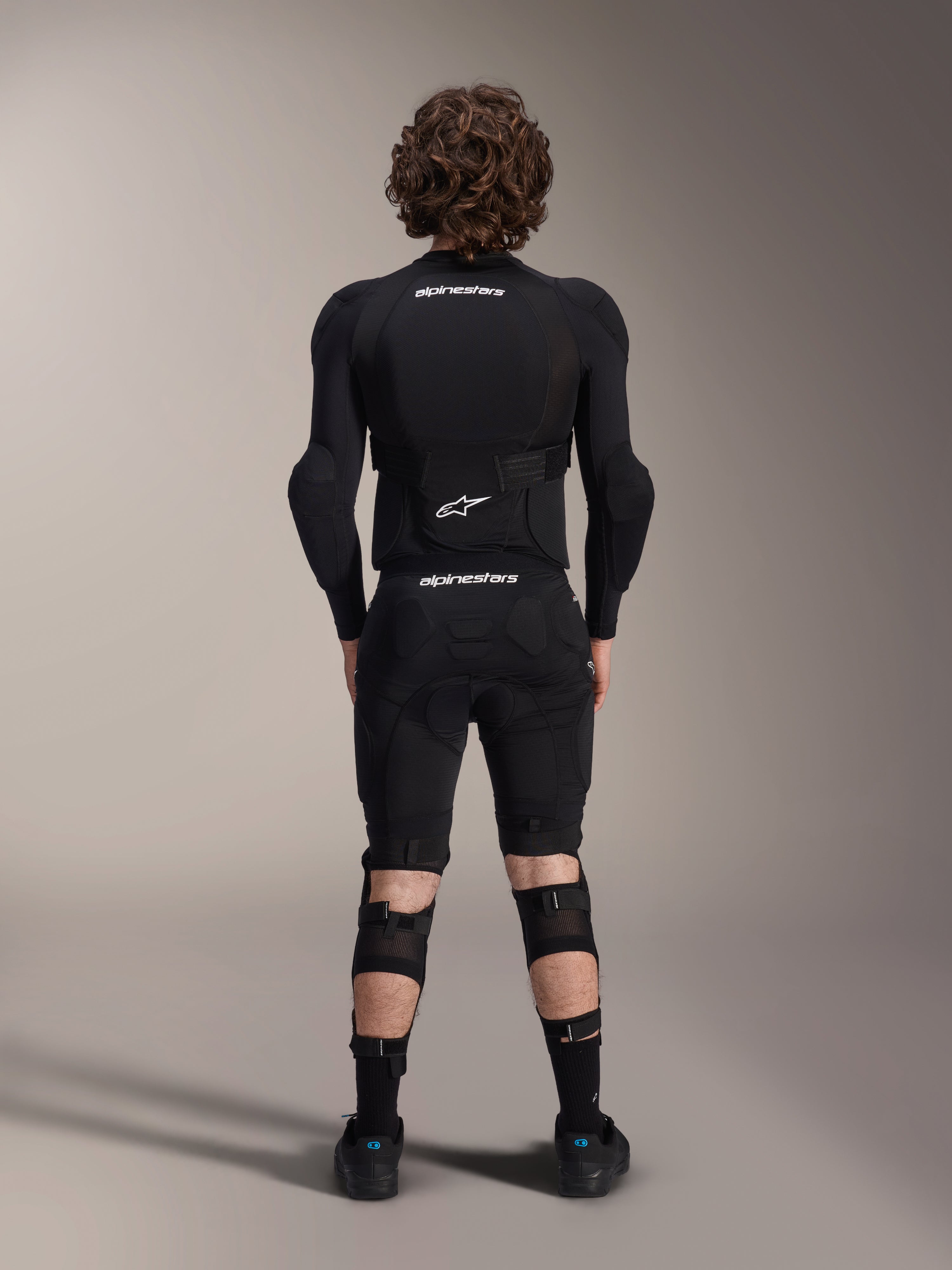 Chaqueta de protección Alpinestars A-Impact Plasma - Manga larga, vista posterior, negra con logotipos blancos de Alpinestars, usada con pantalones cortos de protección y rodilleras para una protección corporal completa de mountain bike