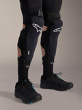 Rodilleras Alpinestars A-Impact Plasma Pro, negro y blanco, con logotipos de la tecnología Nucleon PLASMA, combinadas con calcetines negros y zapatillas de ciclismo de montaña negras, correas seguras de gancho y bucle, equipo de protección ergonómico para ciclismo de montaña