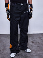 Alpinestars RSRV Arena Suit Pants, pantalones de carreras negros con parches naranjas, logos de McLaren y Alpinestars, persona usando guantes negros y naranjas, zapatos de carreras blancos con detalles negros