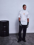 Alpinestars RSRV Pyro SS Tee, camiseta de cuello alto blanca con mangas cortas, logo naranja, estilo urbano premium, persona con guantes negros y pantalones negros