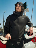 Sudadera con capucha Alpinestars Cypher, forro polar negro con cremallera, capucha de cuello alto con logotipos, pequeño logo Astars blanco en el pecho, combinada con una gorra negra y un piloto que sostiene un casco de motocross blanco, ropa urbana casual de motor