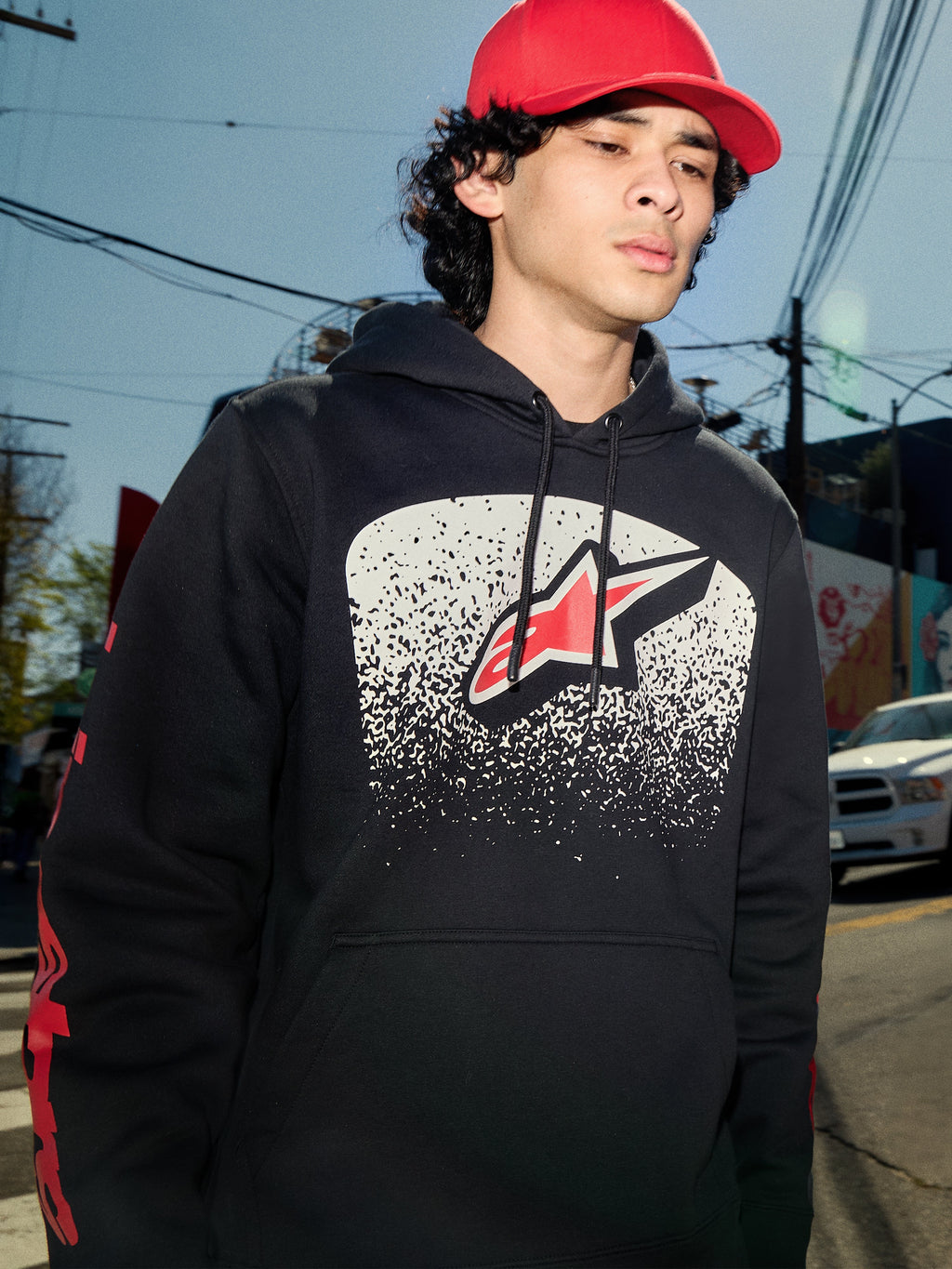 Sudadera con capucha Alpinestars Obsessed, forro polar negro, gráfico en el pecho con degradado MX blanco y logotipo de estrella roja, logotipos rojos en las mangas, ropa urbana casual de inspiración motorsport en un entorno urbano