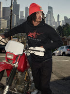 Sudadera con capucha Alpinestars Pulse, negra, sudadera de forro polar con logotipo Astars Combo en rojo y gris, hombre con gorro naranja junto a una motocicleta Honda roja en un entorno urbano, ropa urbana casual de estilo motorsport