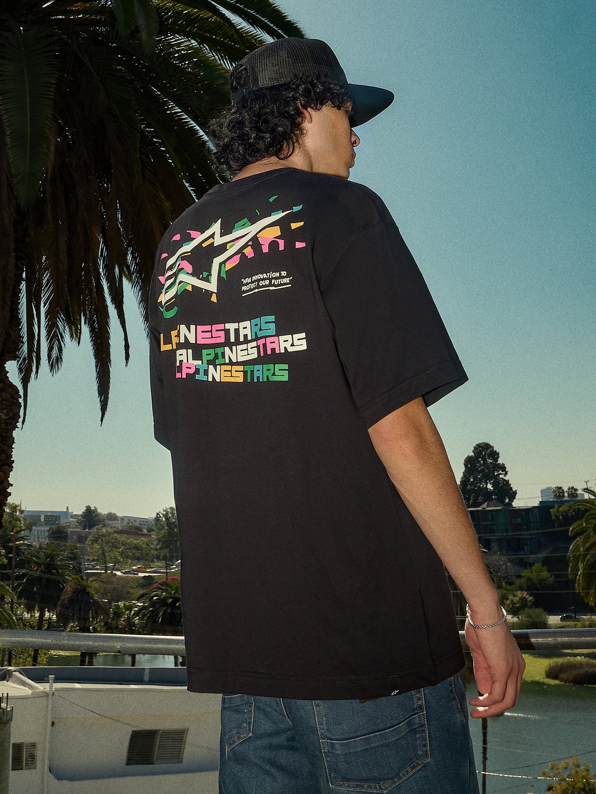 Alpinestars Wild Oversized CSF Tee, camiseta de manga corta, negra, logotipo Astars multicolor vibrante en la espalda, corte de gran tamaño, foto de estilo de vida casual de tipo streetwear con palmeras