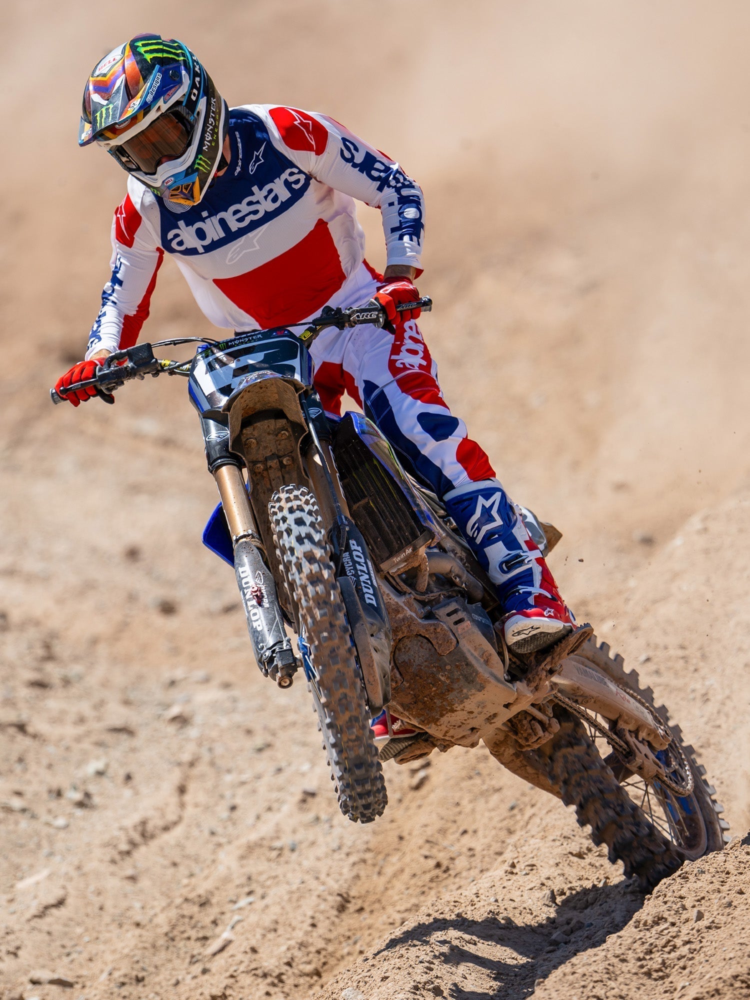 Alpinestars Techstar Fortitude Edición Limitada, pantalones de motocross, en rojo brillante, blanco y azul, usados por un piloto en acción en una pista de tierra, con jersey y botas a juego, equipamiento de carreras off-road de alto rendimiento.