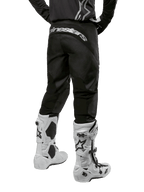 Alpinestars 2024 Fluid Graphite Gear Set, vista posterior de pantalones de motocross negros y grises con el logotipo de Alpinestars en blanco en la zona del asiento, combinados con botas de motocross blancas y negras, equipo especializado para carreras todoterreno