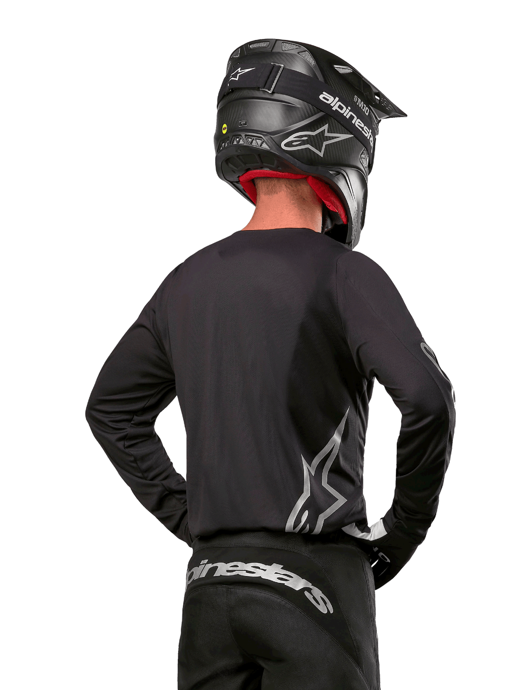 Alpinestars 2024 Fluid Graphite Gear Set, jersey y pantalones de motocross, grafito y plateado, vista trasera con logotipos plateados en la parte baja de la espalda y la cintura, usado con casco negro efecto carbono, diseño de tejido de poliéster ligero para conducción off-road.