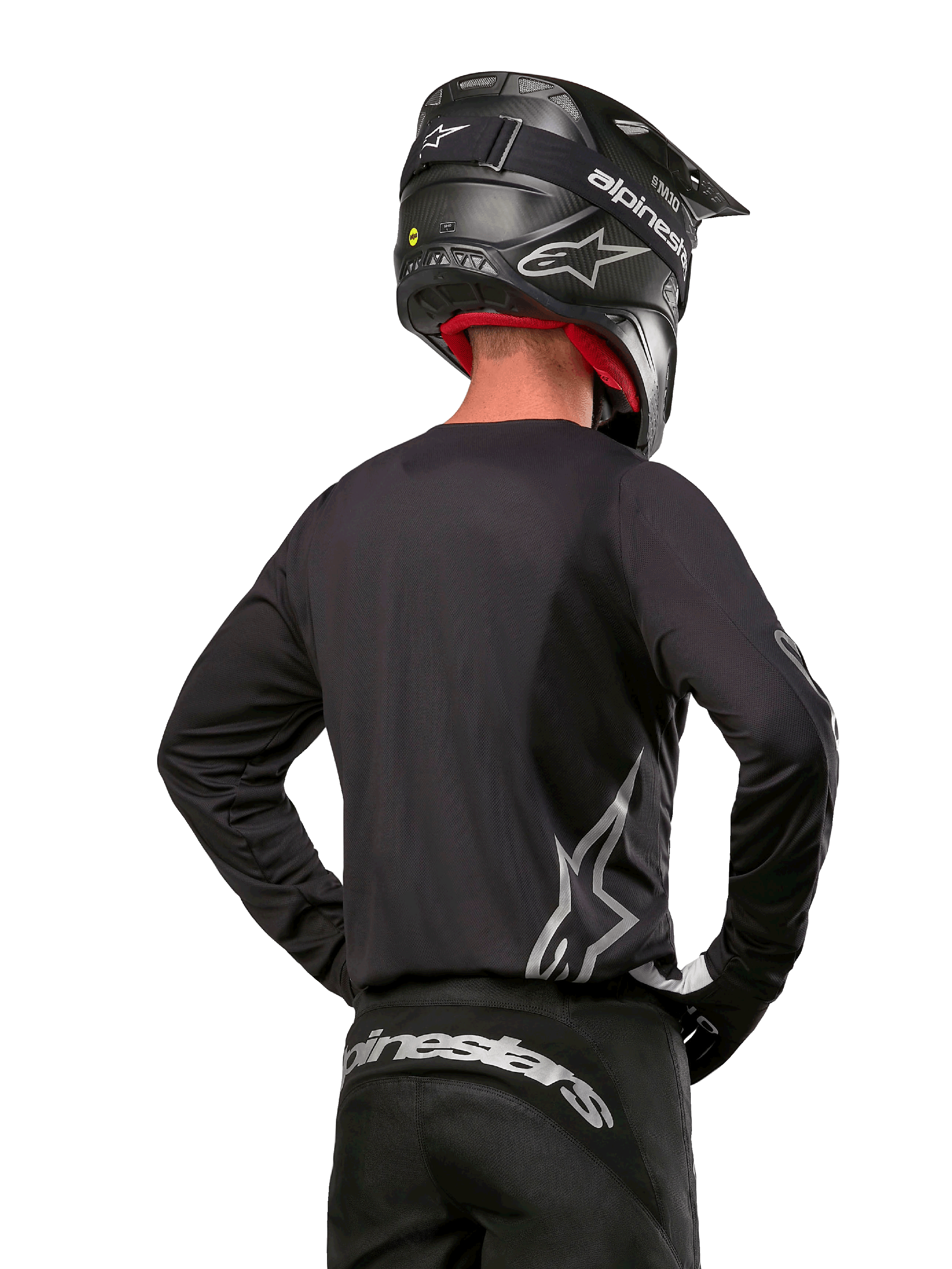 Alpinestars 2024 Fluid Graphite Gear Set, jersey y pantalones de motocross, grafito y plateado, vista trasera con logotipos plateados en la parte baja de la espalda y la cintura, usado con casco negro efecto carbono, diseño de tejido de poliéster ligero para conducción off-road.