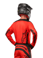 Motocross rider from behind wearing the Alpinestars 2024 Fluid Lurv Jersey in Hot Orange and Black, featuring bold Alpinestars branding on the back and sleeves, paired with matching motocross pants and a black helmet, designed for off-road racing performance.