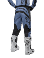 Pantalones Alpinestars Fluid Lurv 2024, pantalones de motocross, azul claro y negro, vista trasera que muestra paneles reforzados negros y logotipo grande de la marca, combinados con botas de motocross blancas y negras, equipamiento de carreras profesional para conducción off-road