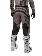 Pantalones Alpinestars Fluid Lurv 2024, pantalones de motocross, Mud Black, vista trasera con gran logotipo negro de Alpinestars en el asiento y paneles negros en las pantorrillas, combinados con botas de motocross blancas y negras y jersey a juego