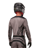 Piloto de motocross visto desde atrás con el jersey Alpinestars 2024 Fluid Lurv en color Mud Black, con logotipos negros de Alpinestars en las mangas y la espalda, combinado con un casco negro y equipamiento a juego para carreras off-road