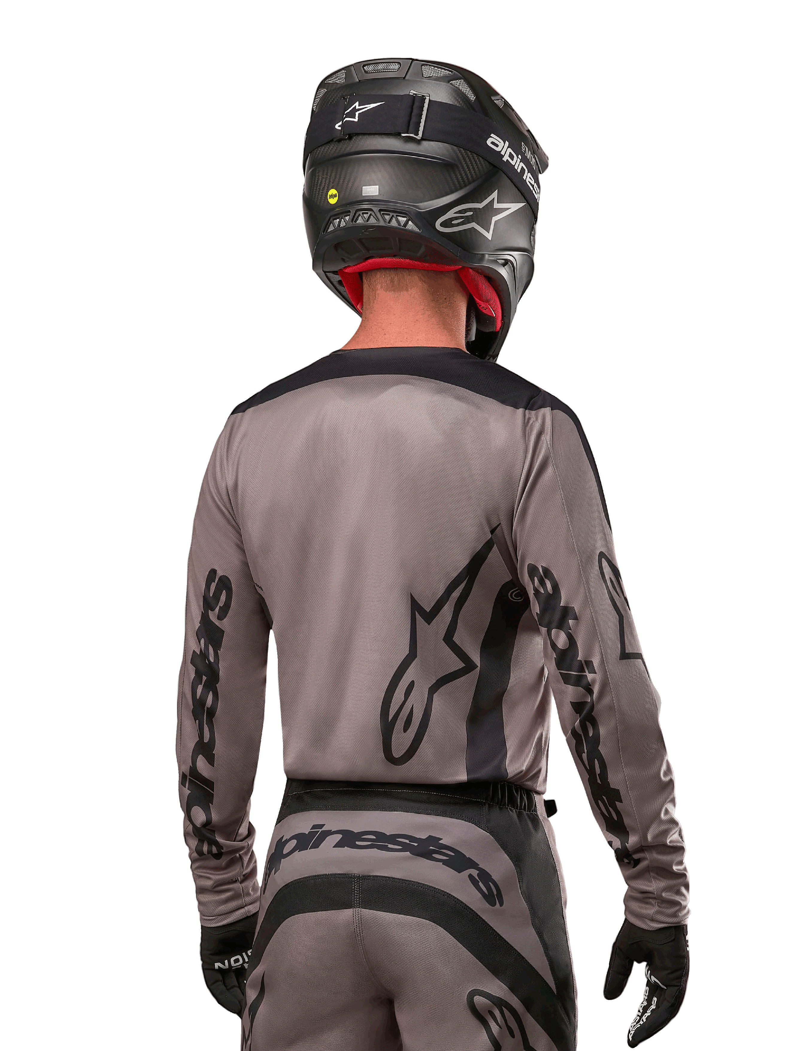Piloto de motocross visto desde atrás con el jersey Alpinestars 2024 Fluid Lurv en color Mud Black, con logotipos negros de Alpinestars en las mangas y la espalda, combinado con un casco negro y equipamiento a juego para carreras off-road