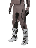 Alpinestars 2024 Fluid Lurv Pants, pantalones de motocross, negro barro y negro, con el logo de Alpinestars, usados con guantes negros y botas de motocross blancas, diseño deportivo para carreras todoterreno