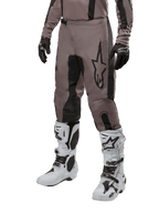 Alpinestars 2024 Fluid Lurv Pants, pantalones de motocross, negro barro y negro, con el logo de Alpinestars, usados con guantes negros y botas de motocross blancas, diseño deportivo para carreras todoterreno
