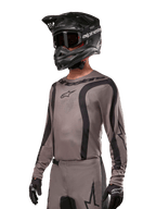 Alpinestars 2024 Fluid Lurv Jersey, jersey de motocross, negro y gris, diseño de manga larga con rayas negras curvas y logotipos, usado con pantalones a juego y un casco de motocross negro, conjunto coordinado para carreras off-road