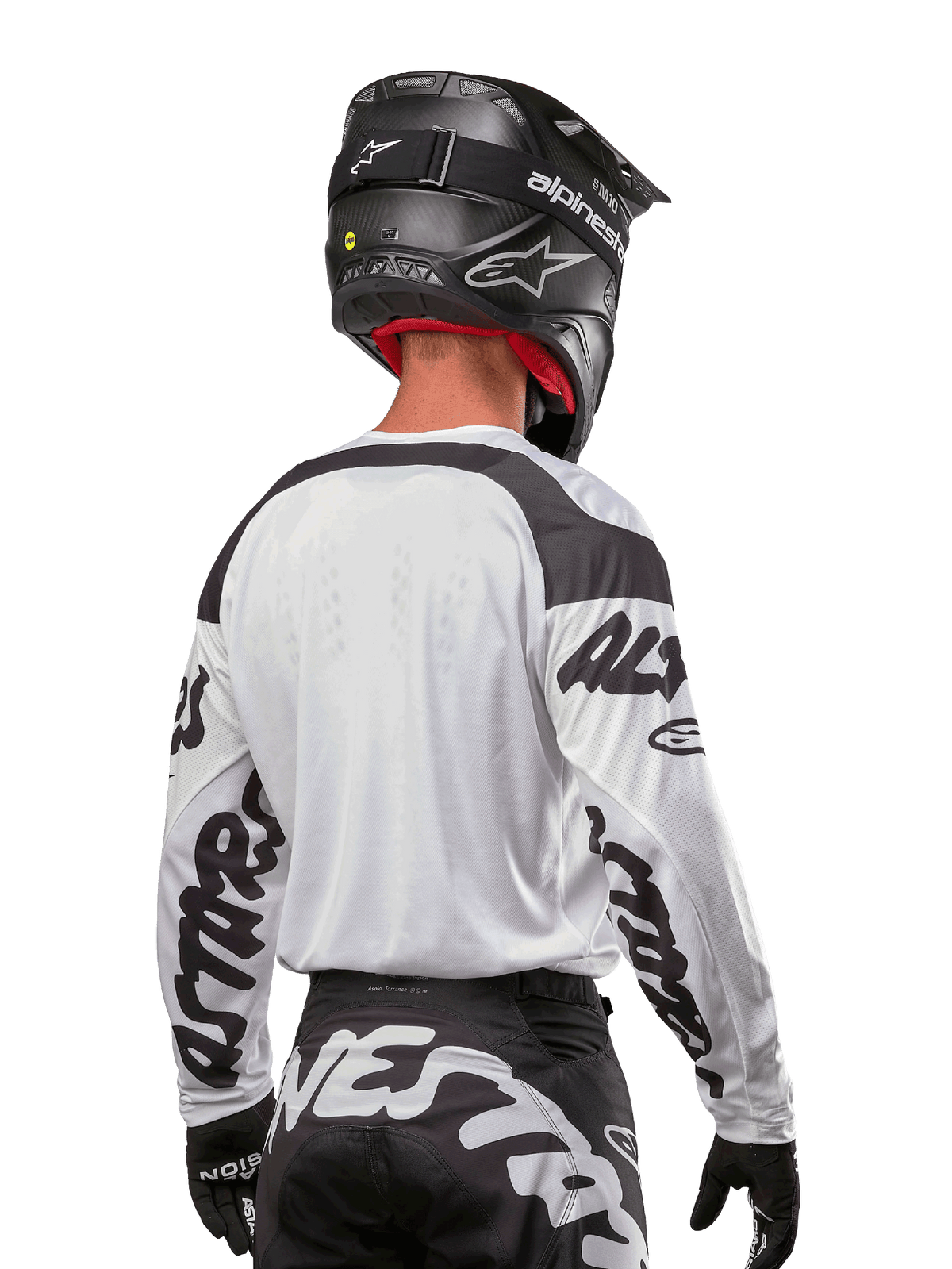 Jersey Alpinestars Racer Hana 2024, blanco y negro, vista posterior que muestra el ajuste ergonómico y la llamativa marca en las mangas, combinado con un casco de motocross negro y pantalones a juego en blanco y negro, equipamiento de alto rendimiento para conducción off-road