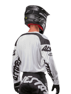 Jersey Alpinestars Racer Hana 2024, blanco y negro, vista posterior que muestra el ajuste ergonómico y la llamativa marca en las mangas, combinado con un casco de motocross negro y pantalones a juego en blanco y negro, equipamiento de alto rendimiento para conducción off-road
