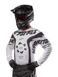 Alpinestars 2024 Racer Hana Jersey, camiseta de motocross, blanca y negra, gráficos llamativos con logotipos de Alpinestars y Astars, usada con casco negro y guantes negros, equipo de alto rendimiento para motocross todoterreno