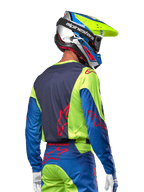 Piloto de motocross vistiendo el jersey Alpinestars 2024 Racer Hoen en amarillo flúor y azul marino, con un logotipo de estrella roja en la espalda, pantalones de motocross a juego y casco de carreras coordinado, vista trasera que muestra el diseño ergonómico para rendimiento todoterreno.