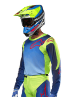 Jersey Alpinestars Racer Hoen 2024, camiseta de motocross, en color amarillo flúor y azul Night Navy con logos rojos, combinada con un casco a juego en amarillo, azul y rojo y guantes azules; equipamiento vibrante para carreras off-road