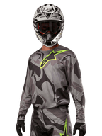 Alpinestars 2024 Racer Tactical Jersey, jersey de motocross, camuflaje Cast Gray Camo Magnet con logo verde neón, usado con casco blanco y negro y guantes negros, tejido técnico que absorbe la humedad para carreras fuera de carretera