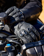 Guantes Alpinestars SP X 7, guantes de moto de cuero perforado negro con protectores de nudillos de TPU y deslizadores en los dedos, mostrados en las manos de un piloto sujetando el manillar de una motocicleta.