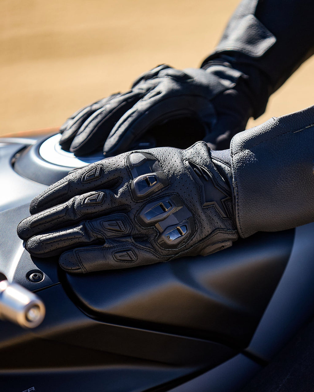 Guantes Alpinestars SP X 7, negros, guantes de moto de puño corto con cuero perforado, manos apoyadas sobre un depósito de combustible oscuro, con protección de nudillos de TPU de doble densidad visible y marca en relieve, diseñados para conducción deportiva y de carretera.