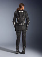 Traje de cuero de 2 piezas Alpinestars Stella GP-R7, traje de moto para mujer, negro con detalles blancos, vista trasera que muestra la joroba aerodinámica GP-R7 y la marca Tech-Air Ready, logotipos blancos de Alpinestars en las mangas, paneles elásticos de acordeón, usado con botas de carreras negras