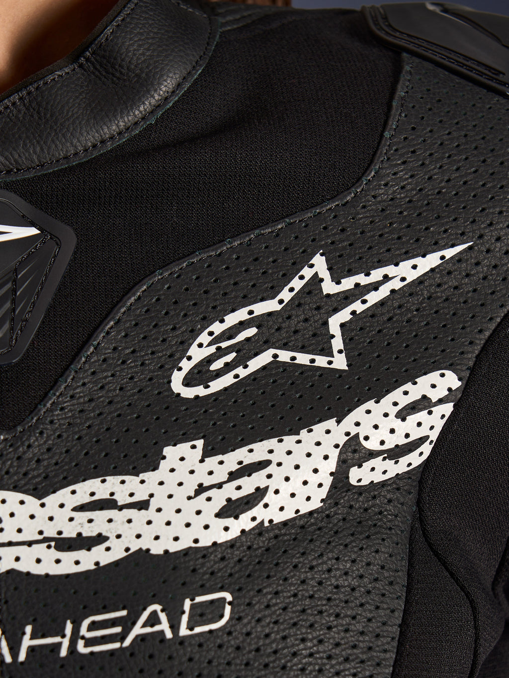 Primer plano del traje de cuero de 2 piezas Alpinestars Stella GP-R7 en color negro, con paneles de cuero perforado, un gran logotipo blanco de Alpinestars en el pecho y secciones de tejido elástico transpirable.