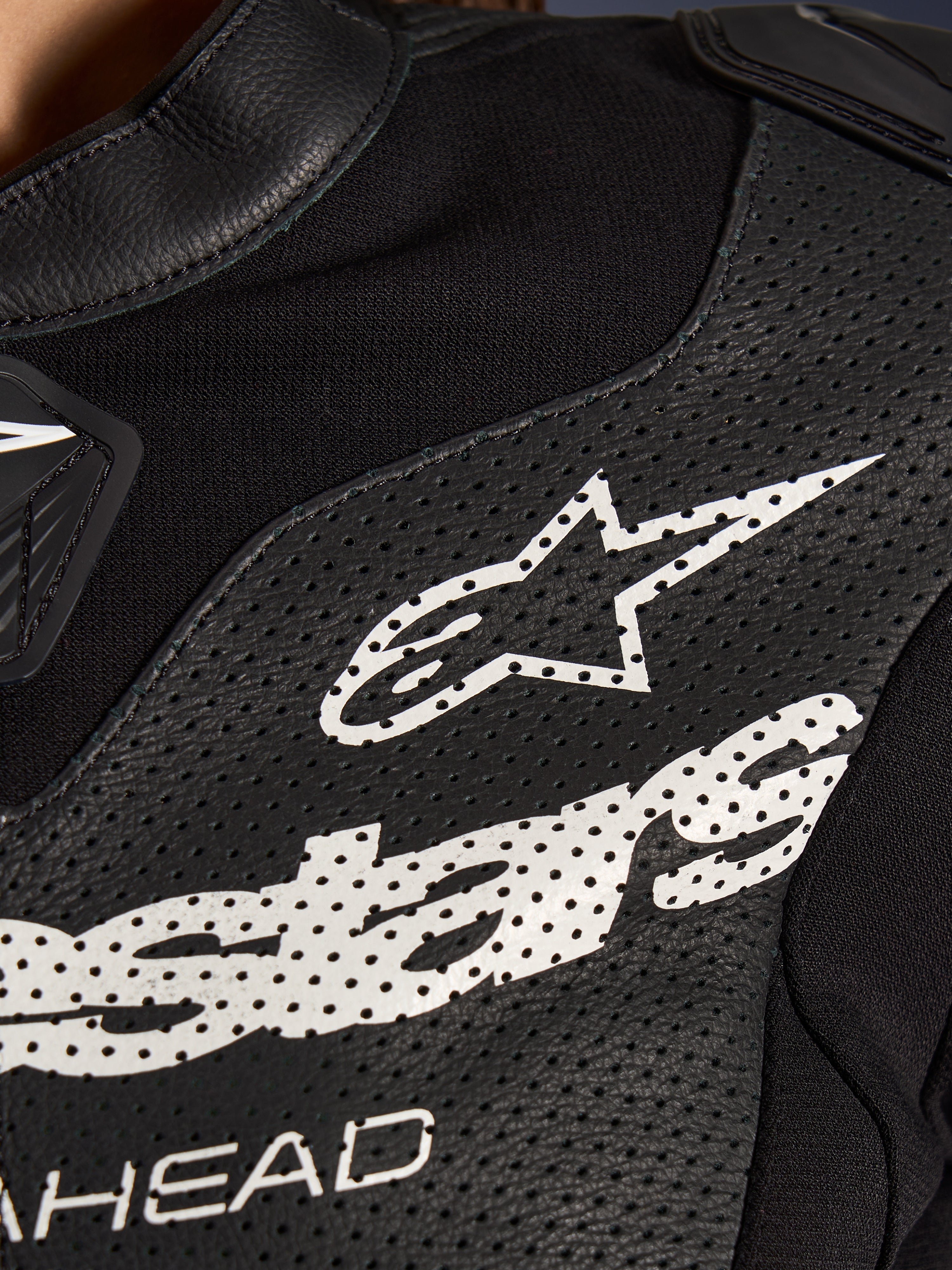 Primer plano del traje de cuero de 2 piezas Alpinestars Stella GP-R7 en color negro, con paneles de cuero perforado, un gran logotipo blanco de Alpinestars en el pecho y secciones de tejido elástico transpirable.