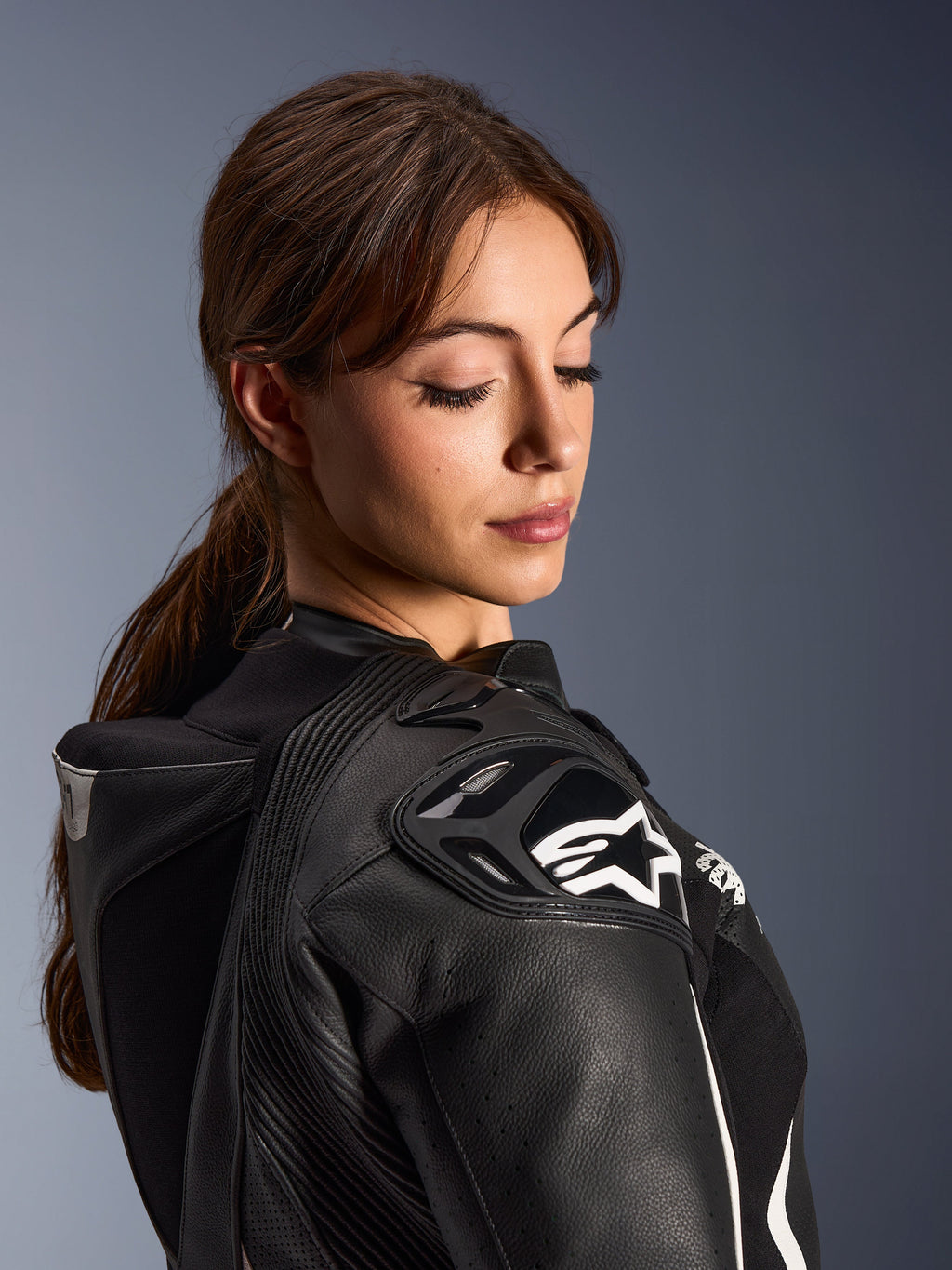 Mujer con el traje de cuero de 2 piezas Alpinestars Stella GP-R7, primer plano del hombro de cuero negro con protección DFS RR y logo de estrella blanca, que incluye la joroba aerodinámica integrada y detalles perforados.