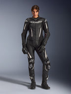 Mujer con el traje de cuero de 2 piezas Alpinestars Stella GP-R7 en negro con detalles blancos, paneles de cuero perforado y logotipos blancos en el pecho y las rodillas, combinado con guantes y botas de carreras negros a juego, equipamiento profesional de competición para motociclismo