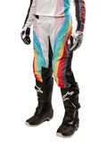 Alpinestars Stella Techstar 2024, pantalones de motocross para mujer, negro multicolor con franjas diagonales rojas, amarillas y azules, combinados con botas de montar negras y guantes blancos, con paneles protectores negros en las rodillas y marca llamativa para carreras fuera de pista