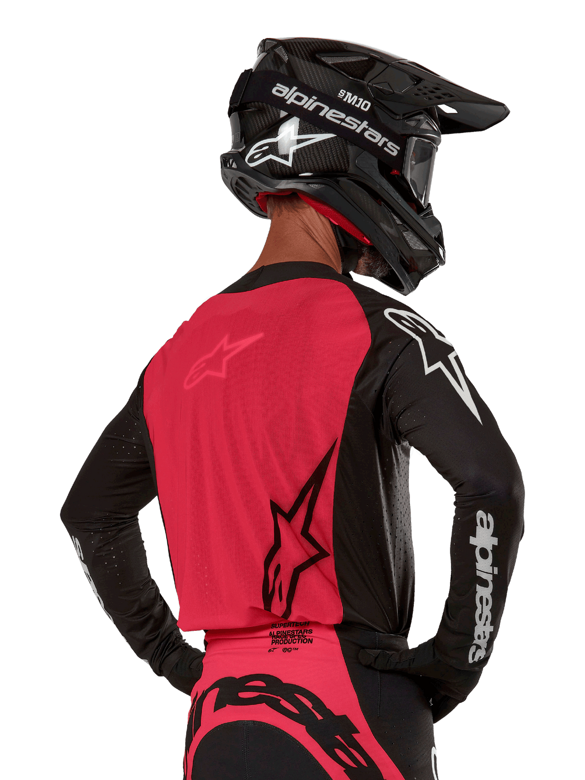 Alpinestars 2024 Supertech Ward Jersey, jersey de motocross, negro y rojo berry, vista posterior con panel de malla roja y mangas negras con logotipos blancos, usado con casco de fibra de carbono negro y guantes, ajuste de carrera atlético para conducción todoterreno