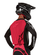 Alpinestars 2024 Supertech Ward Jersey, jersey de motocross, negro y rojo berry, vista posterior con panel de malla roja y mangas negras con logotipos blancos, usado con casco de fibra de carbono negro y guantes, ajuste de carrera atlético para conducción todoterreno