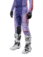Alpinestars 2024 Techstar Ocuri Pants, pantalones de motocross para hombre, color púrpura con detalles en naranja vibrante y logos rojos, diseño ergonómico con paneles elásticos, combinados con botas blancas de motocross y guantes negros.