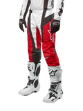 Alpinestars Techstar Ocuri Pants 2024, pantalones de carreras de motocross, rojo Marte, blanco y negro, usados con camiseta blanca y negra a juego, guantes negros y botas de carreras blancas con hebillas, equipo de protección técnica mostrado sobre un fondo blanco.