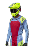 Jersey Techstar Ocuri 2024, jersey de carreras de motocross, azul claro con detalles en rojo y amarillo flúor, usado con casco amarillo neón a juego y gafas negras, con logotipos negros de Alpinestars en el pecho y los hombros, diseño atlético inspirado en las carreras para rendimiento todoterreno