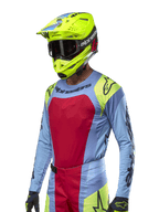 Jersey Techstar Ocuri 2024, jersey de carreras de motocross, azul claro con detalles en rojo y amarillo flúor, usado con casco amarillo neón a juego y gafas negras, con logotipos negros de Alpinestars en el pecho y los hombros, diseño atlético inspirado en las carreras para rendimiento todoterreno