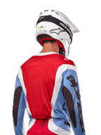 Alpinestars 2024 Techstar Ocuri Jersey, jersey de motocross, azul claro, rojo Marte y blanco, vista trasera del piloto con casco blanco a juego y gafas negras, con marca negra llamativa en las mangas y ajuste de carrera ergonómico para rendimiento todoterreno.