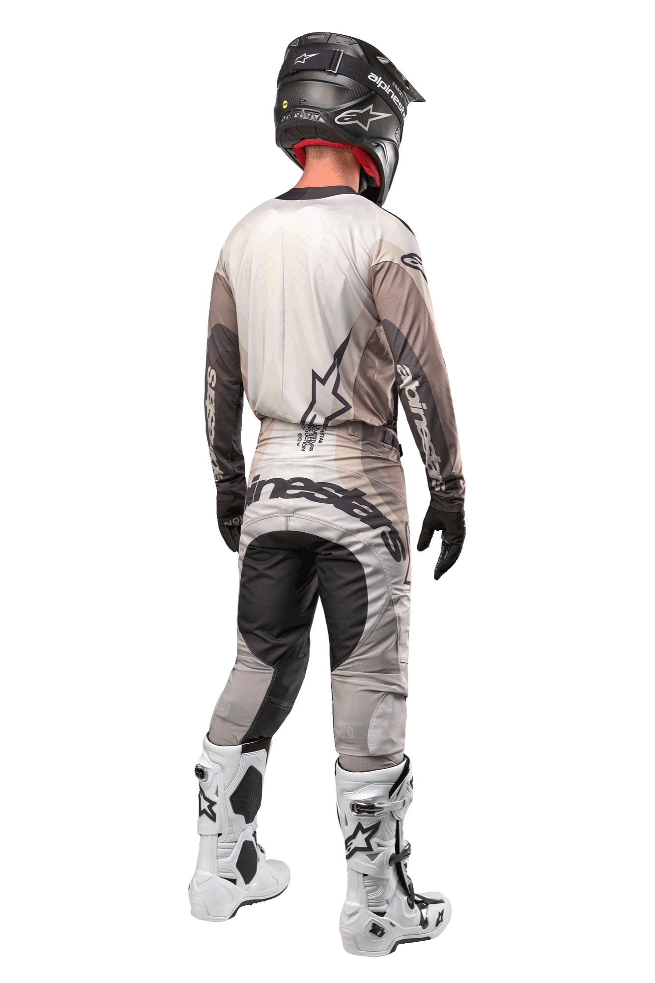 Pantalones Alpinestars Techstar Pneuma 2024, pantalones de motocross, arena oscura y gris polvo de hierro, vista trasera usada por un piloto con jersey a juego, botas blancas y negras y casco negro, con un llamativo logotipo de Alpinestars en el asiento y paneles oscuros reforzados.