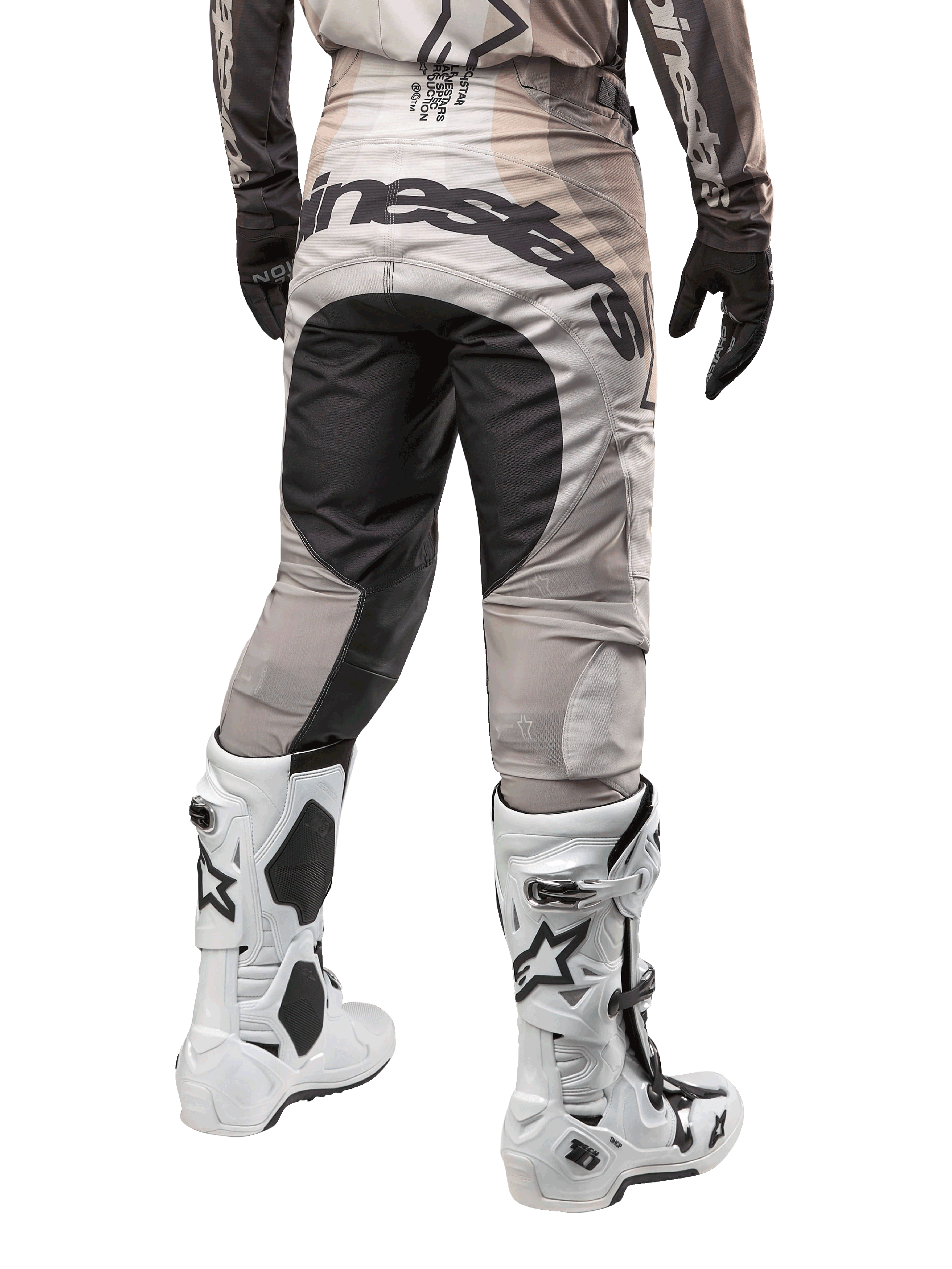 Pantalones Alpinestars Techstar Pneuma 2024, pantalones de motocross, color arena oscura y gris, vista trasera desde la cintura para abajo, logotipo negro de Alpinestars en el asiento, usados con botas de motocross blancas y negras y guantes negros, diseño duradero para competición off-road