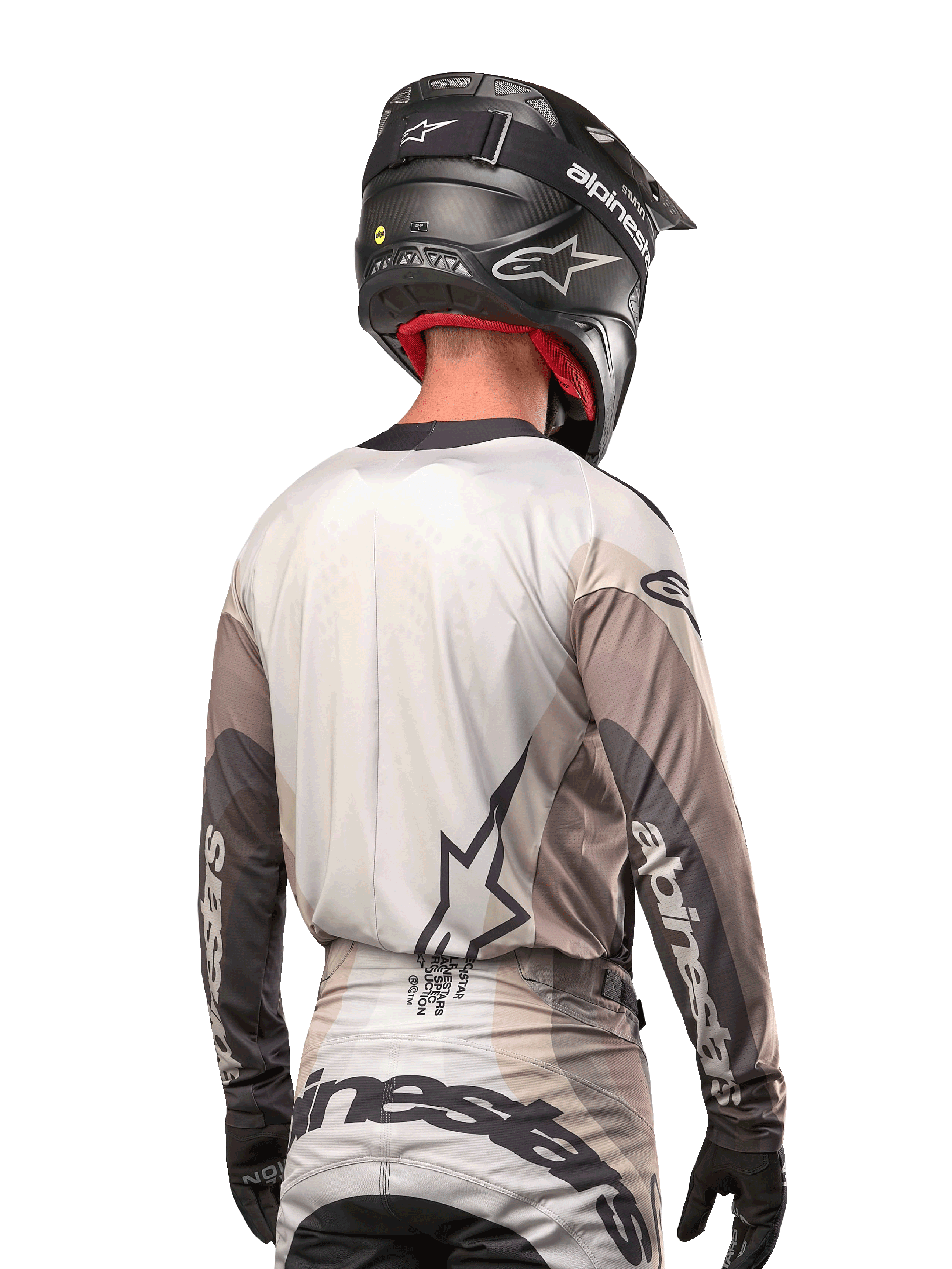 Piloto de motocross visto desde atrás con el Jersey Alpinestars Techstar Pneuma 2024 en gris arena y gris hierro, combinado con un casco negro con acabado de carbono, con un gran logo de estrella en la espalda y la marca Alpinestars en las mangas.