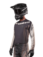Jersey Alpinestars Techstar Pneuma 2024, camiseta de motocross de manga larga, arena oscura y gris, camiseta técnica con perforaciones láser y logotipos blancos, usada con pantalones a juego y casco negro, ajuste atlético para conducción off-road