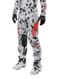 Alpinestars Techstar Rantera 2024, pantalones de motocross, camuflaje gris con patrón abstracto negro y rojo, usados con jersey a juego, guantes negros y botas de motocross blancas, diseñados para carreras todoterreno de alto rendimiento