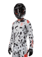 Alpinestars Techstar Rantera Jersey 2024, jersey de motocross en gris con patrones abstractos negros y acentos rojos, diseño de manga larga usado con casco y guantes negros, equipo técnico para carreras todoterreno